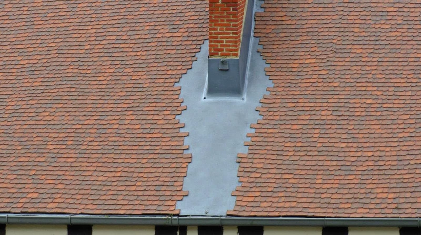 Toiture chartraine en tuile plate, noue en zinc et solin de cheminée en plomb, au-dessus d'un mur à pans de bois