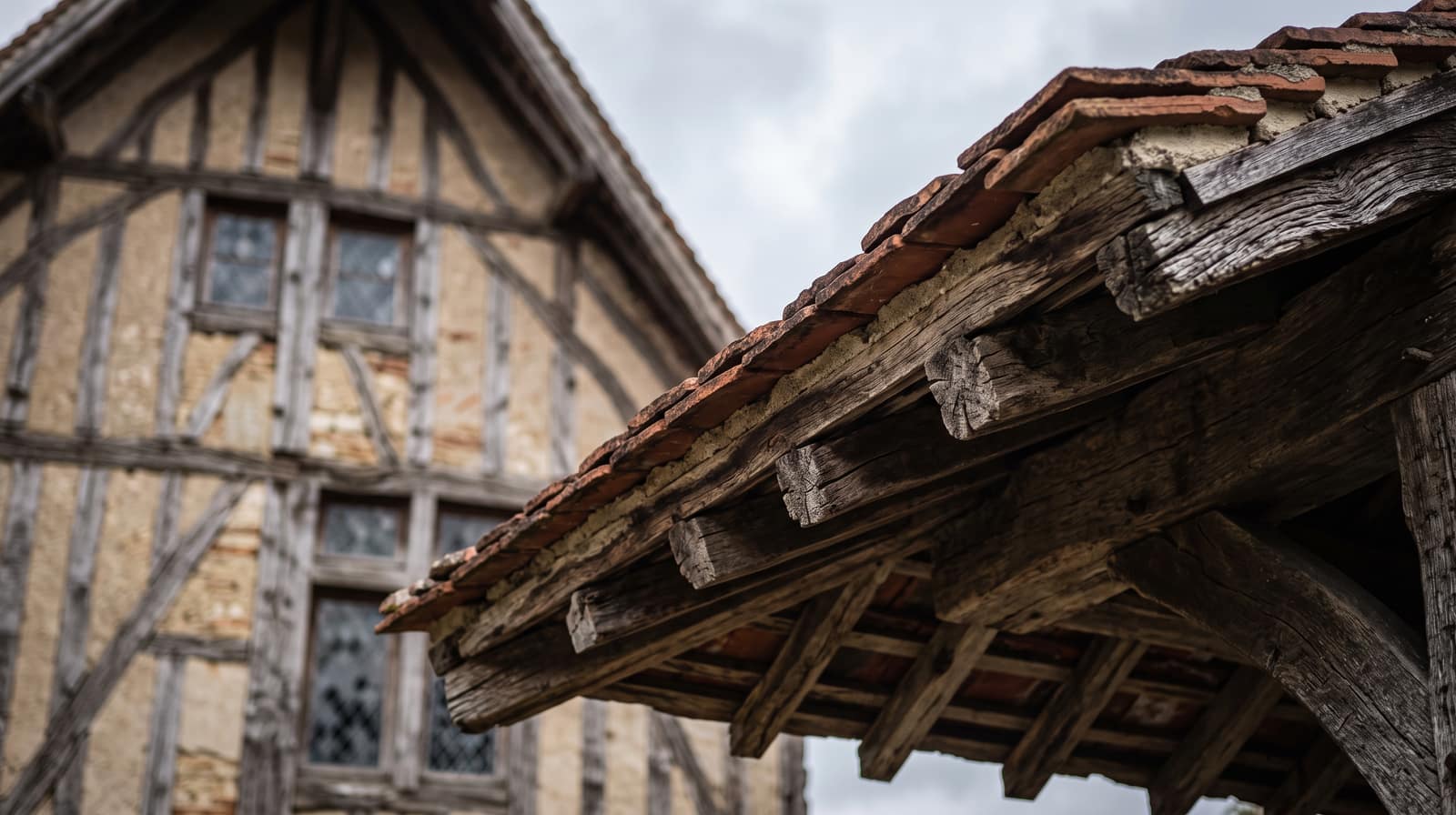 Angle d'un débord de toit en tuile plate avec plusieurs chevrons en bois apparents, sur une maison à pans de bois